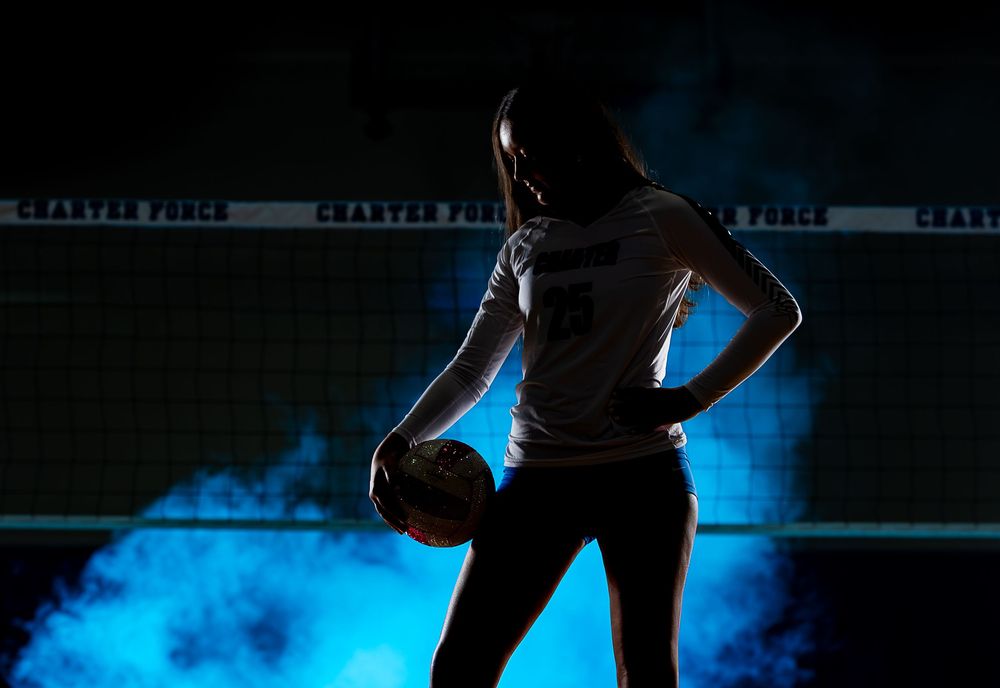 Silhouette of volleyball player holding ball against dark background with dramatic blue smoke effect.