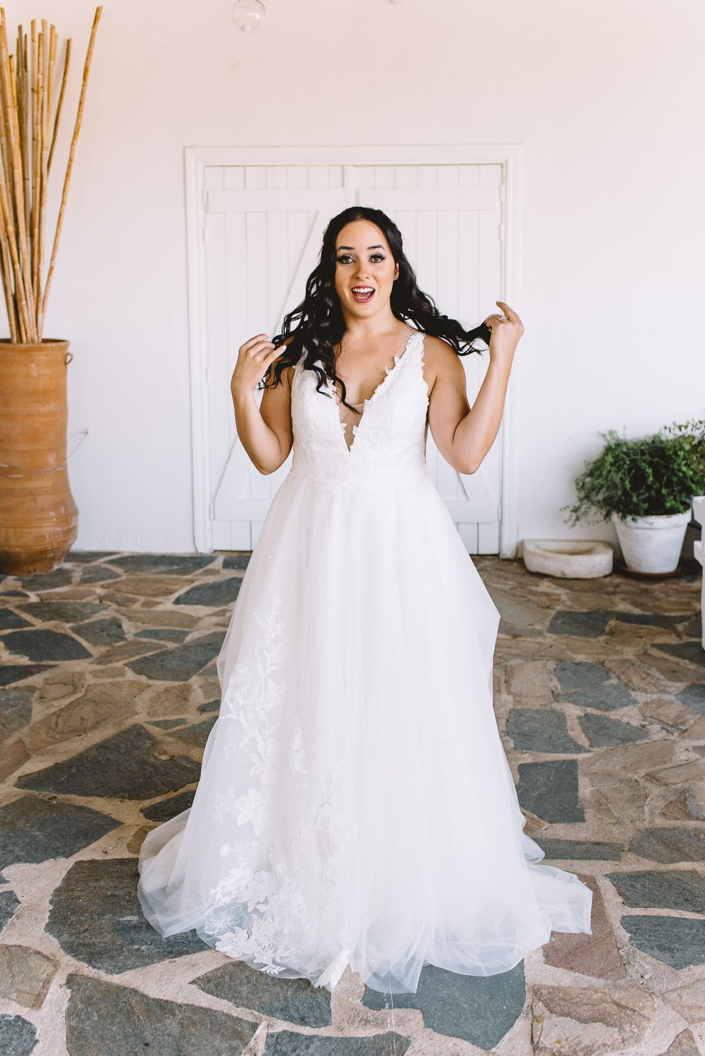 Bride in elegant lace A-line wedding gown poses joyfully on stone patio at Greek venue.