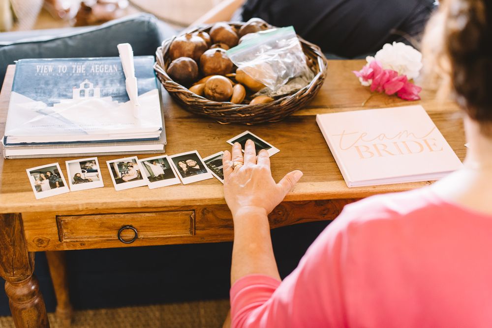 Woman looking at polaroid photos on wooden table with a bride book, basket of rolls, and wedding planning materials.