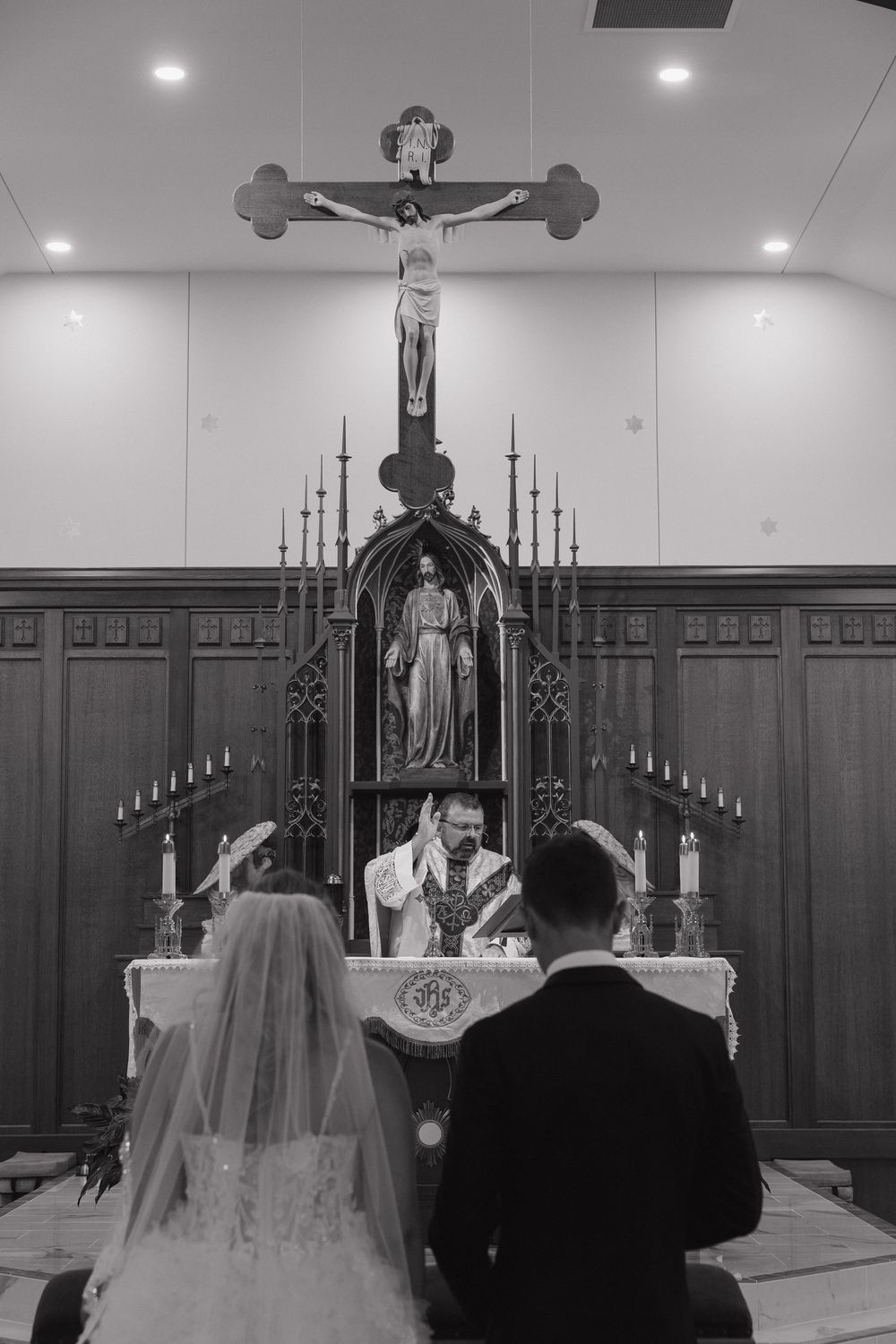 Black and white photo of a bride and groom kneeling at a Catholic church altar during their wedding ceremony.