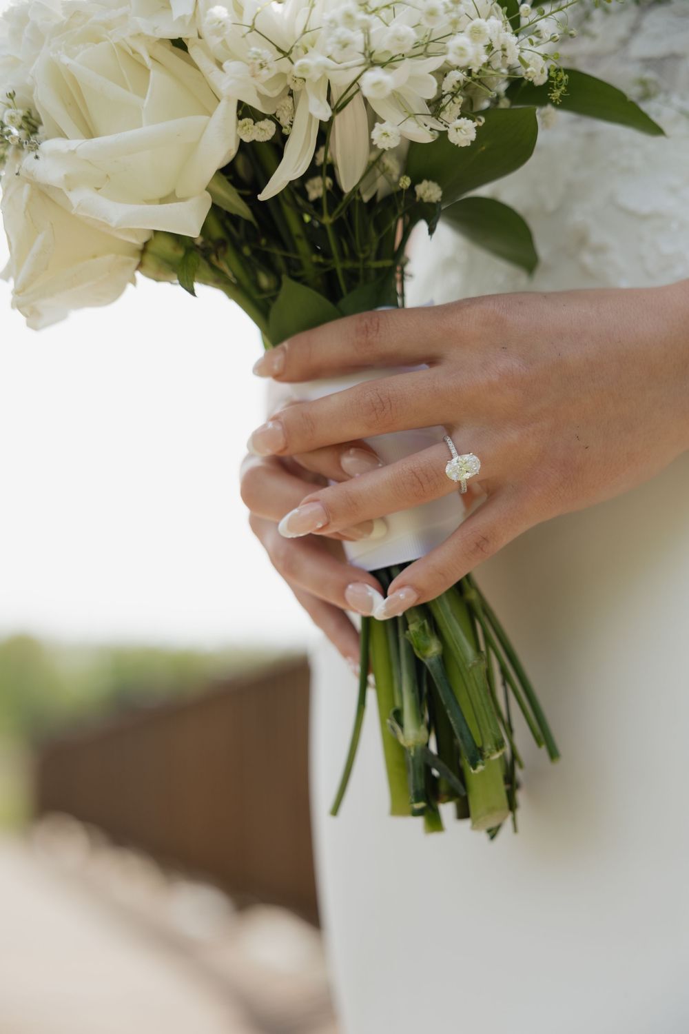 Bride holding white rose bouquet with diamond solitaire engagement ring on her finger.