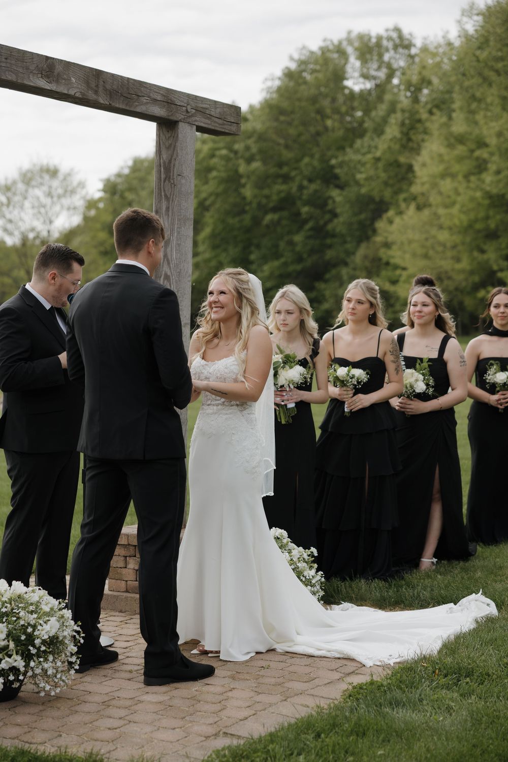 Outdoor wedding ceremony with bride and groom at altar surrounded by bridesmaids in black.