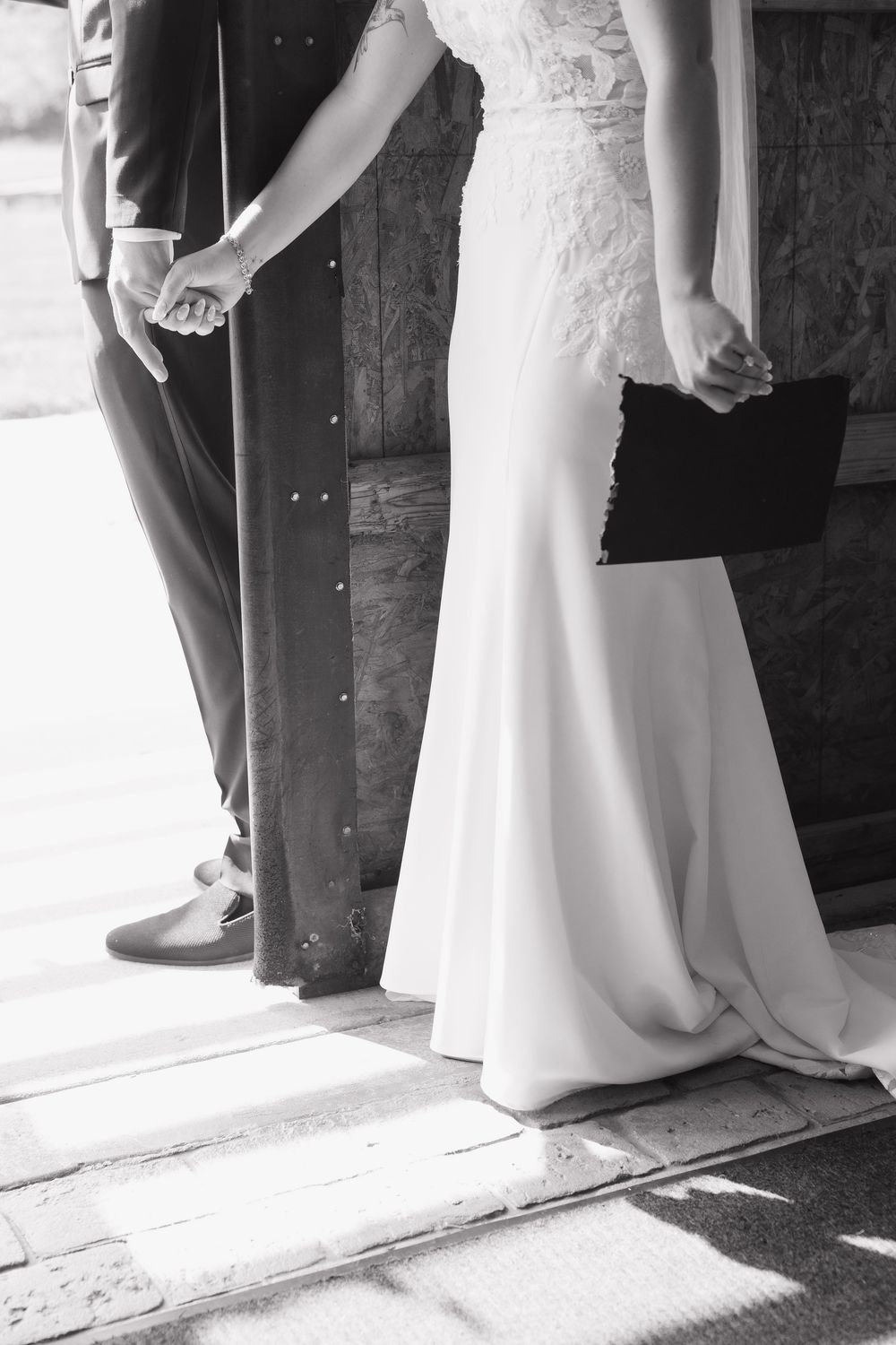 Black and white photo of bride and groom holding hands in elegant wedding attire.