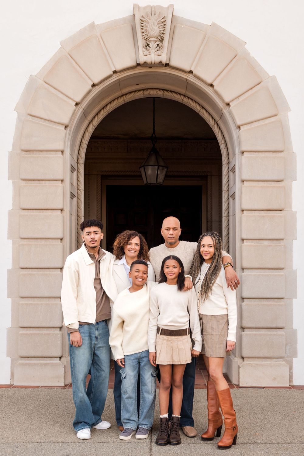 A family of six poses under a stone archway entrance, dressed in coordinating neutral tones for a formal portrait.