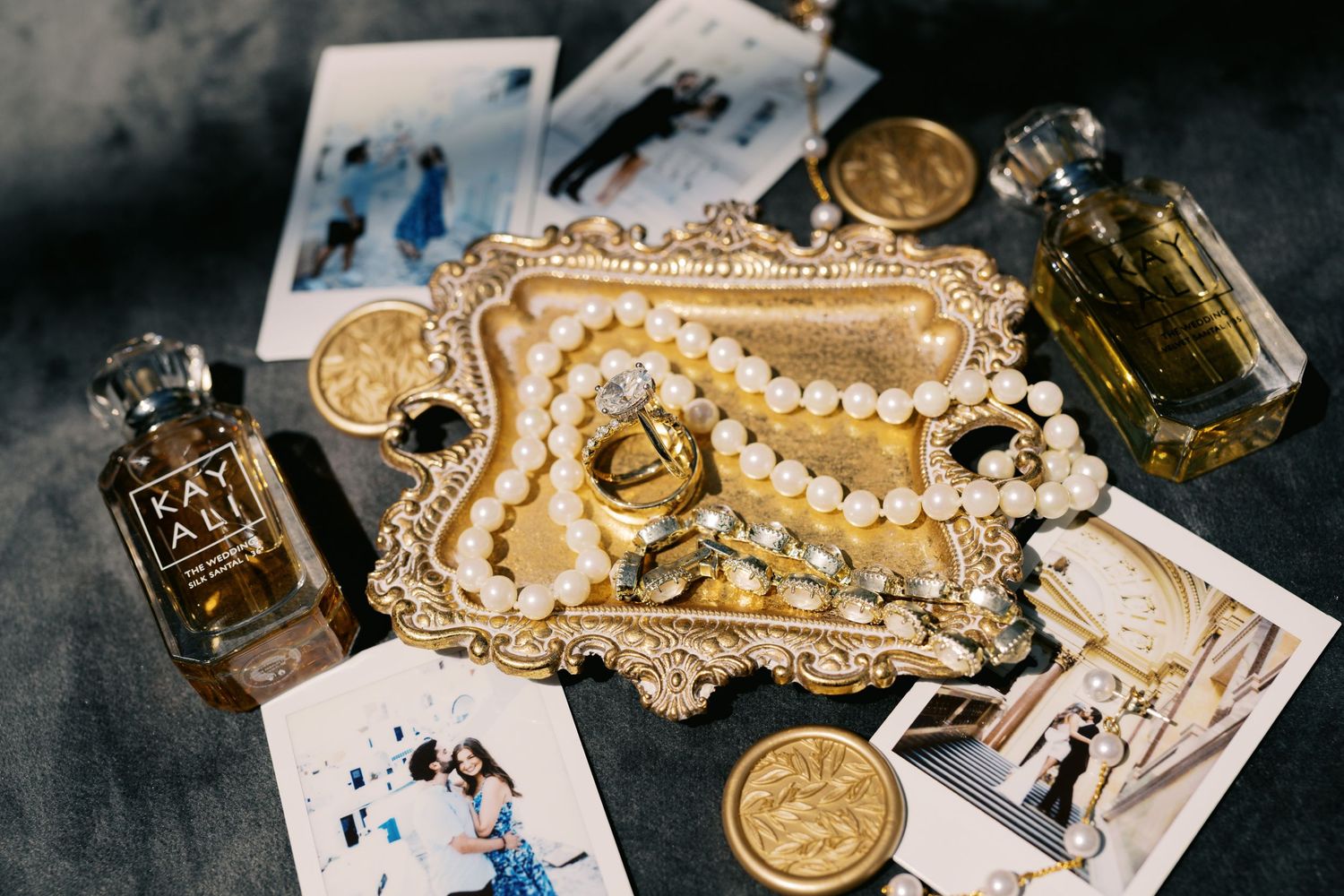 Gold ornate tray with pearl necklace, coins, perfume bottles, and fashion illustrations on gray surface.
