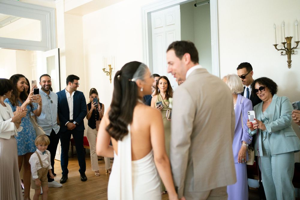 Bride and groom enter wedding reception as guests celebrate and take photos in elegant white venue.