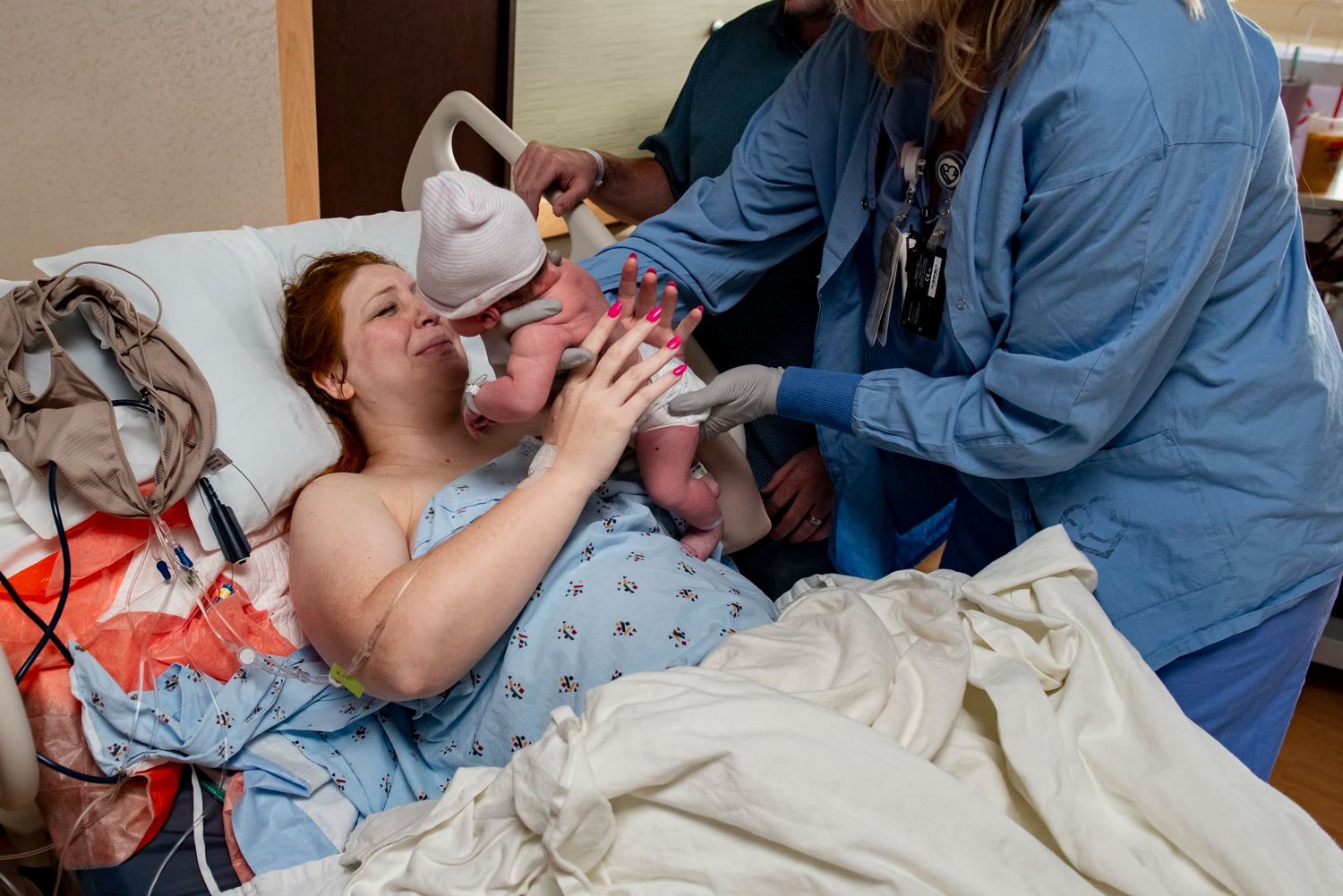 Healthcare workers assist with newborn care in a hospital room setting.