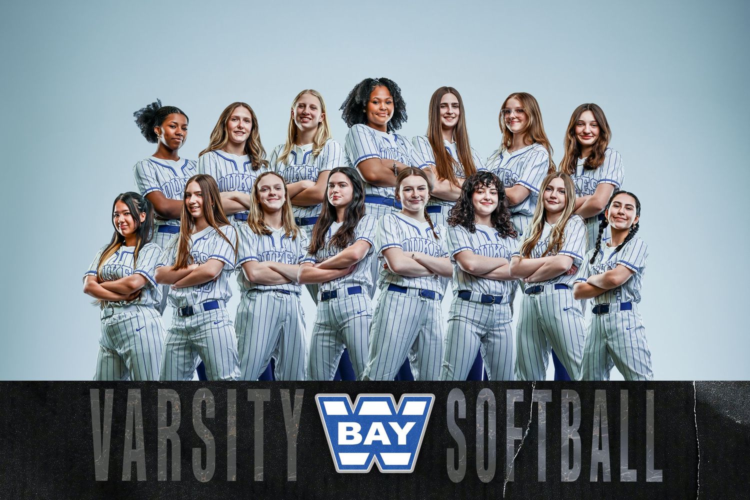Womens softball team poses in white pinstripe uniforms with arms crossed for an official team photo.
