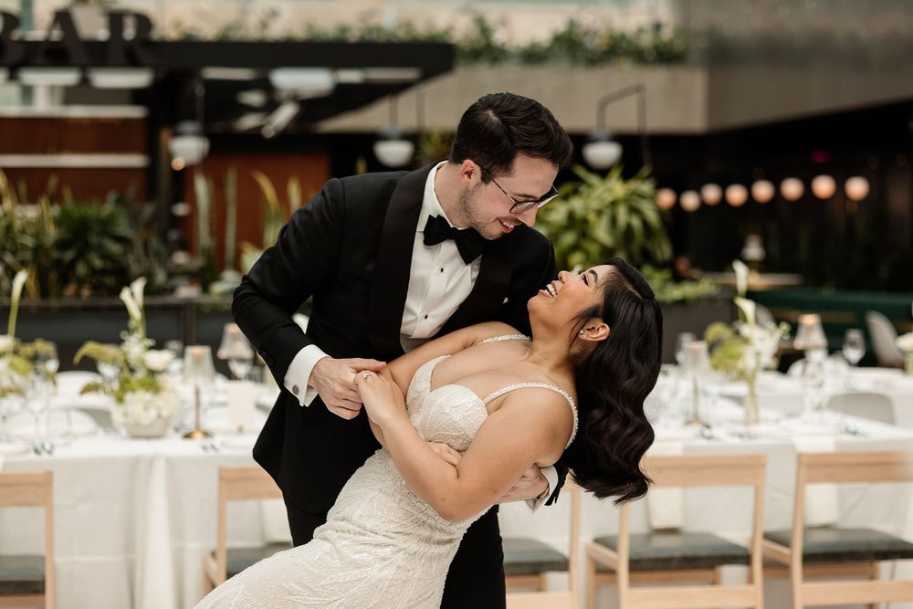 Aliza Dworkind candidly captures as groom dips bride in a romantic wedding dance pose surrounded by elegant white wedding reception.