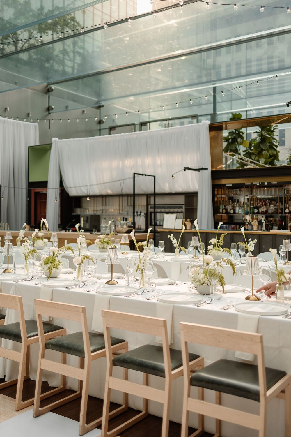 Elegant wedding reception table with white linens, floral centerpieces, and light wood chairs in the modern Le Cathcart wedding venue Mtl.