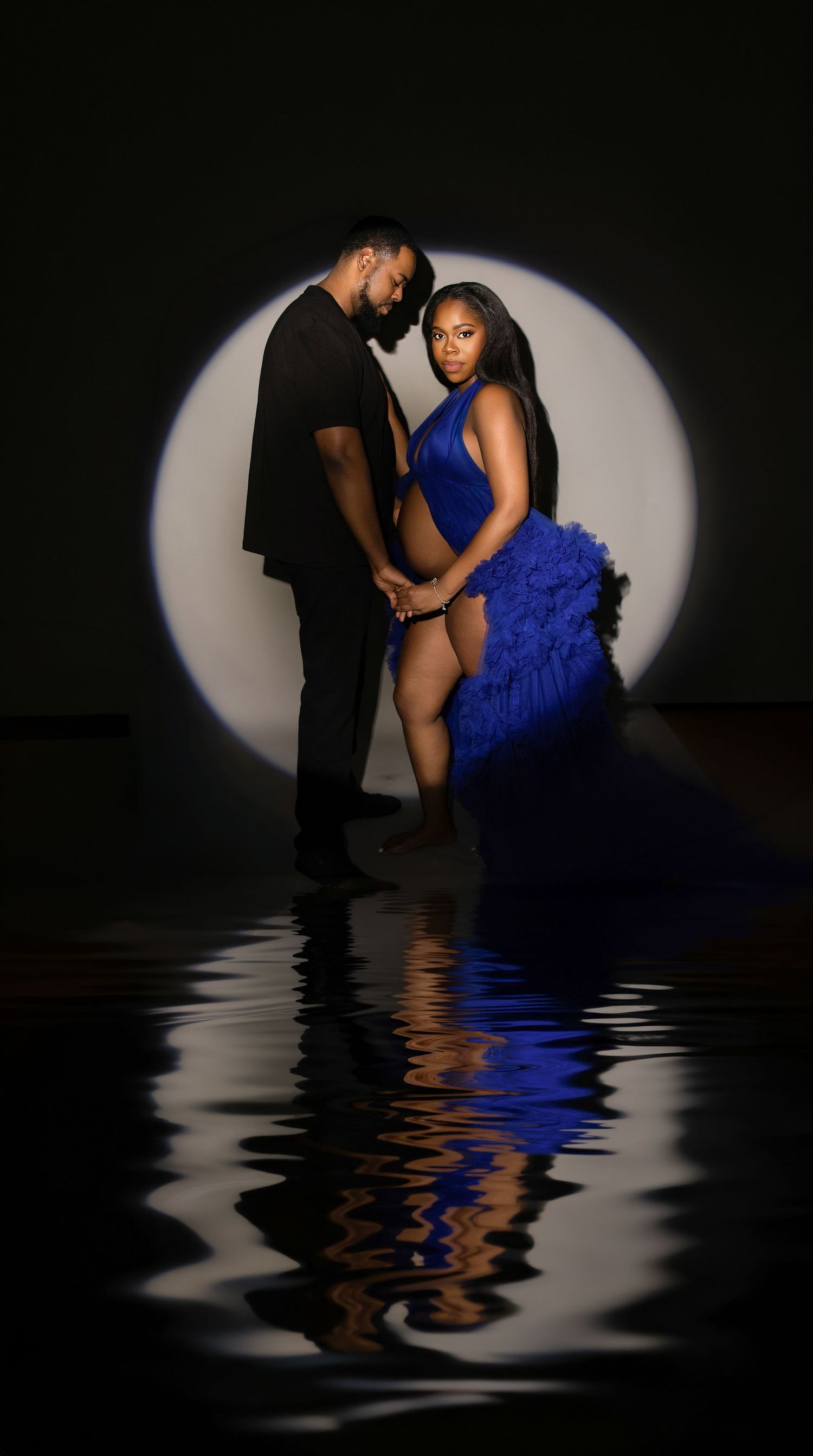 Pregnant woman in flowing satin gown posing gracefully in a studio with reflective floor. at Vanessa Charlotte Photography  Wolverhampton