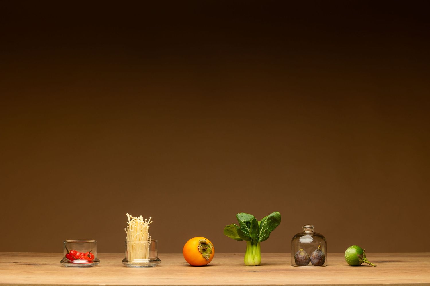Minimalist arrangement of fresh vegetables and ingredients on a wooden surface against a brown background.