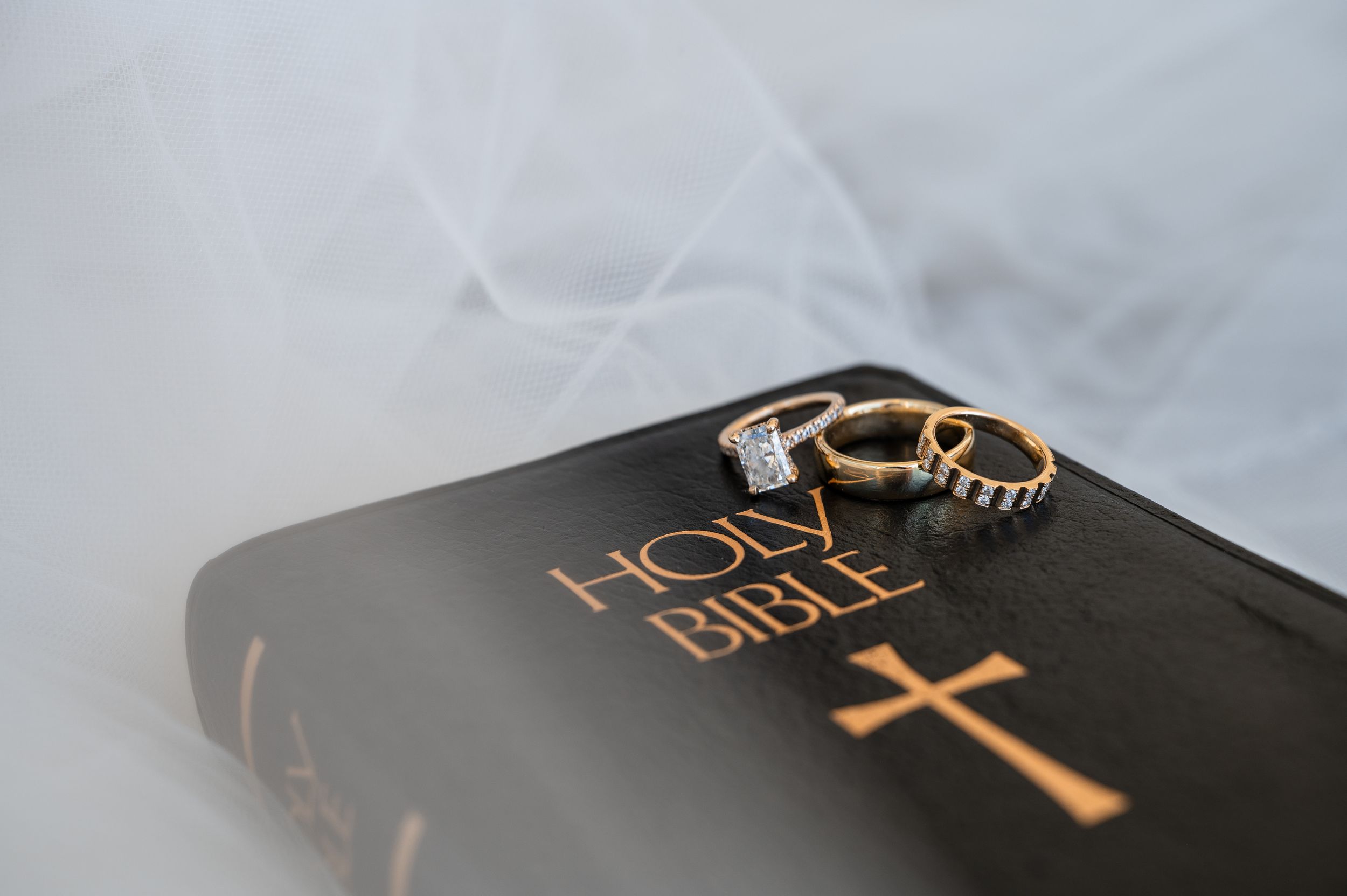 Wedding rings resting on a Holy Bible with gold cross, symbolizing faith and marriage commitment.