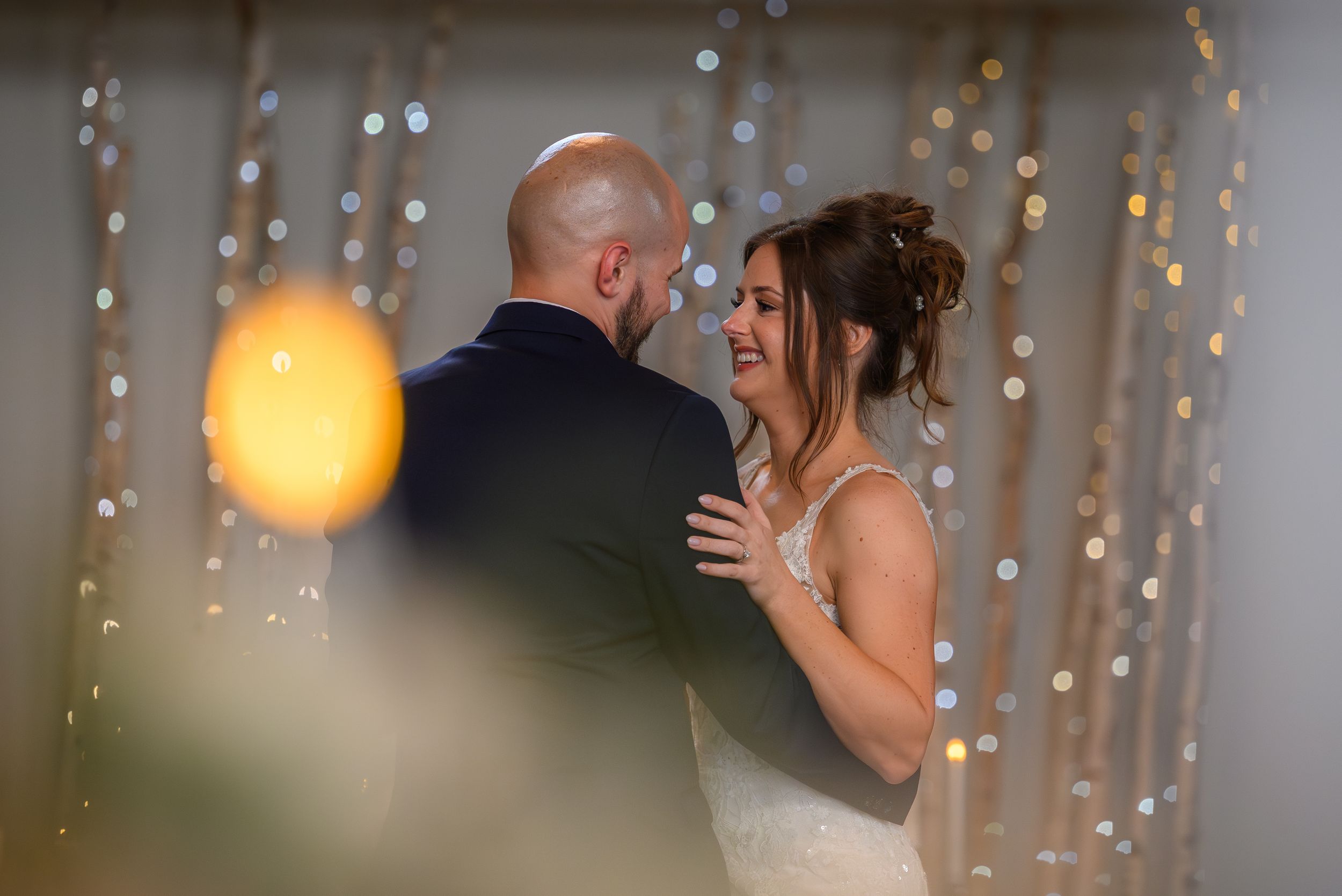 A bride and groom share a joyful first dance surrounded by sparkling bokeh lights at their wedding reception.