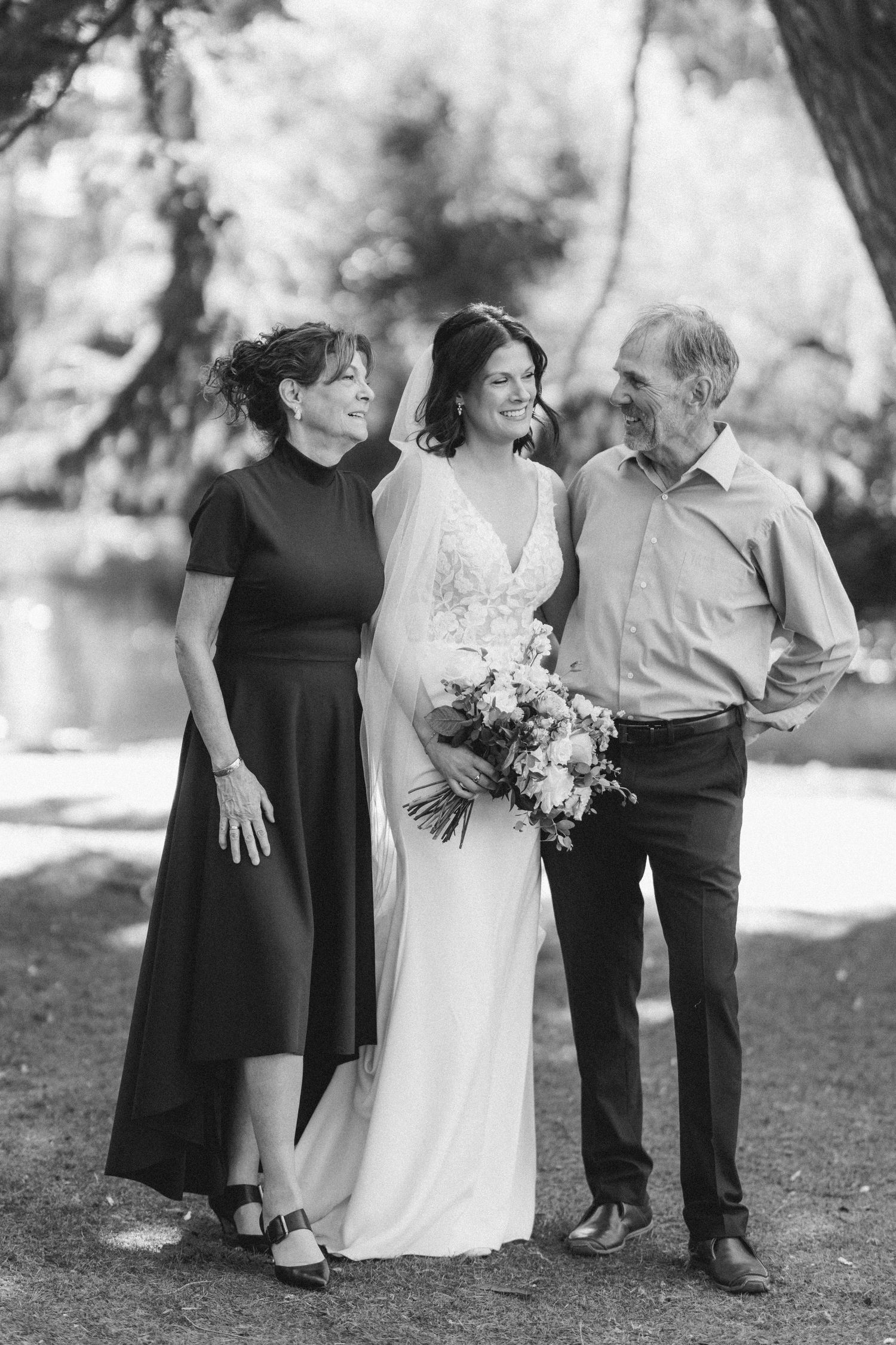 Bride with parents in black and white wedding portrait outdoors.