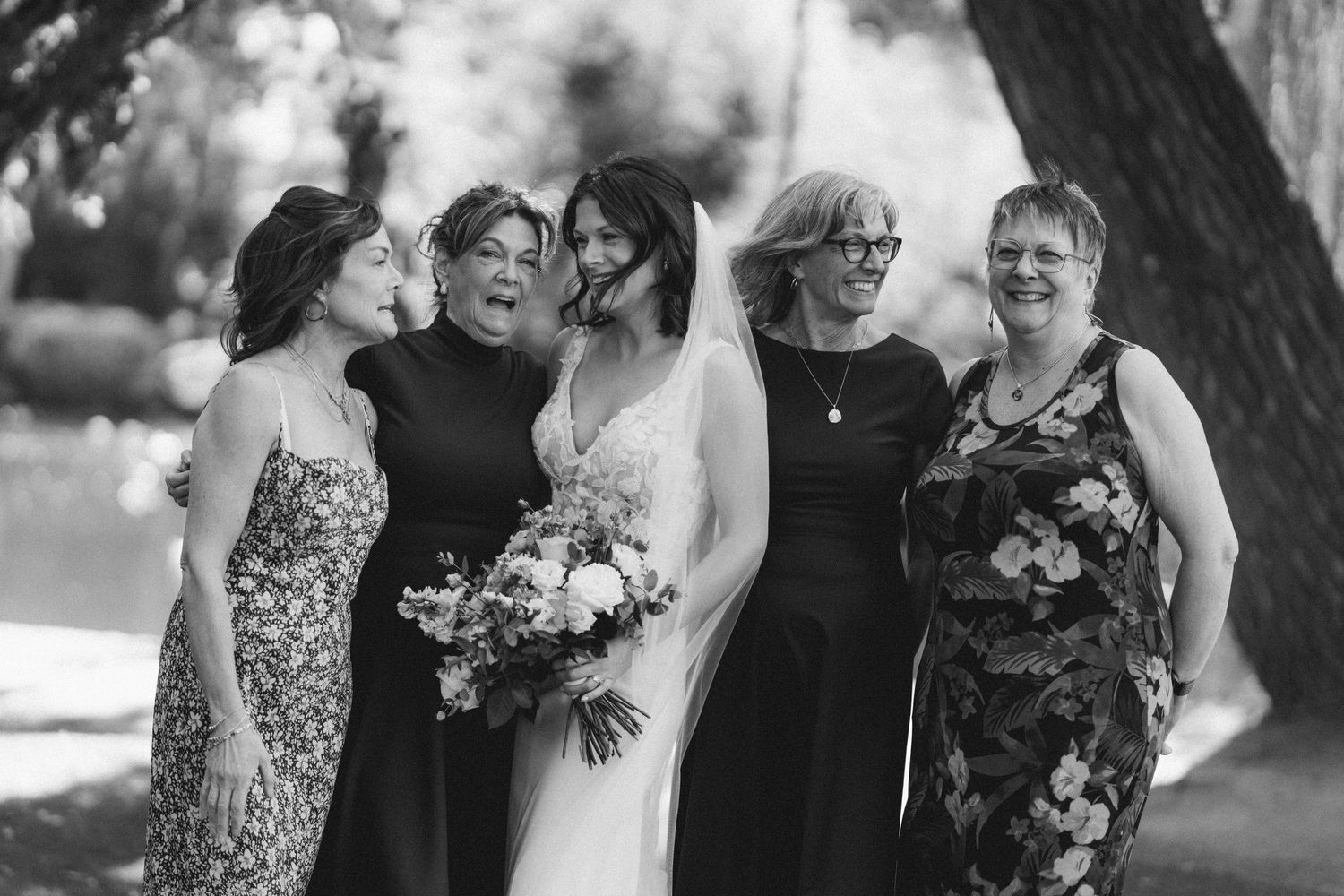 Bride with bouquet posing with four women outdoors in black and white wedding portrait.