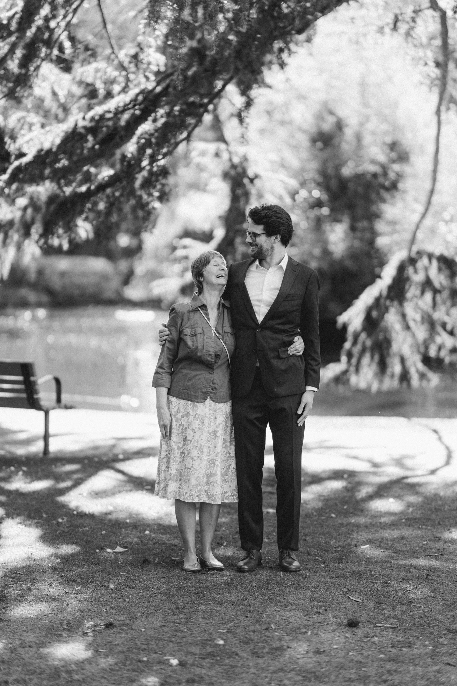 Black and white portrait of an elderly woman and young man smiling together in a sunlit park.
