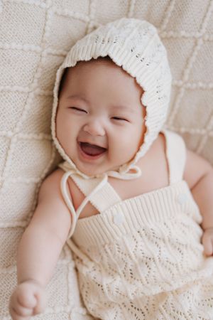 A happy baby wearing a white knit bonnet and lace outfit smiles joyfully in a series of connected photos.在一組連貫的照片中，一個戴著白色針織帽、穿著蕾絲衣服的快樂寶寶