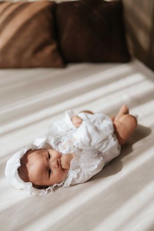 A sleeping baby wearing white clothing lies peacefully on white bedding in a series of progressive photos.一組連續的照片顯示，一個穿著白色衣服的嬰兒安詳地躺在白色的床單