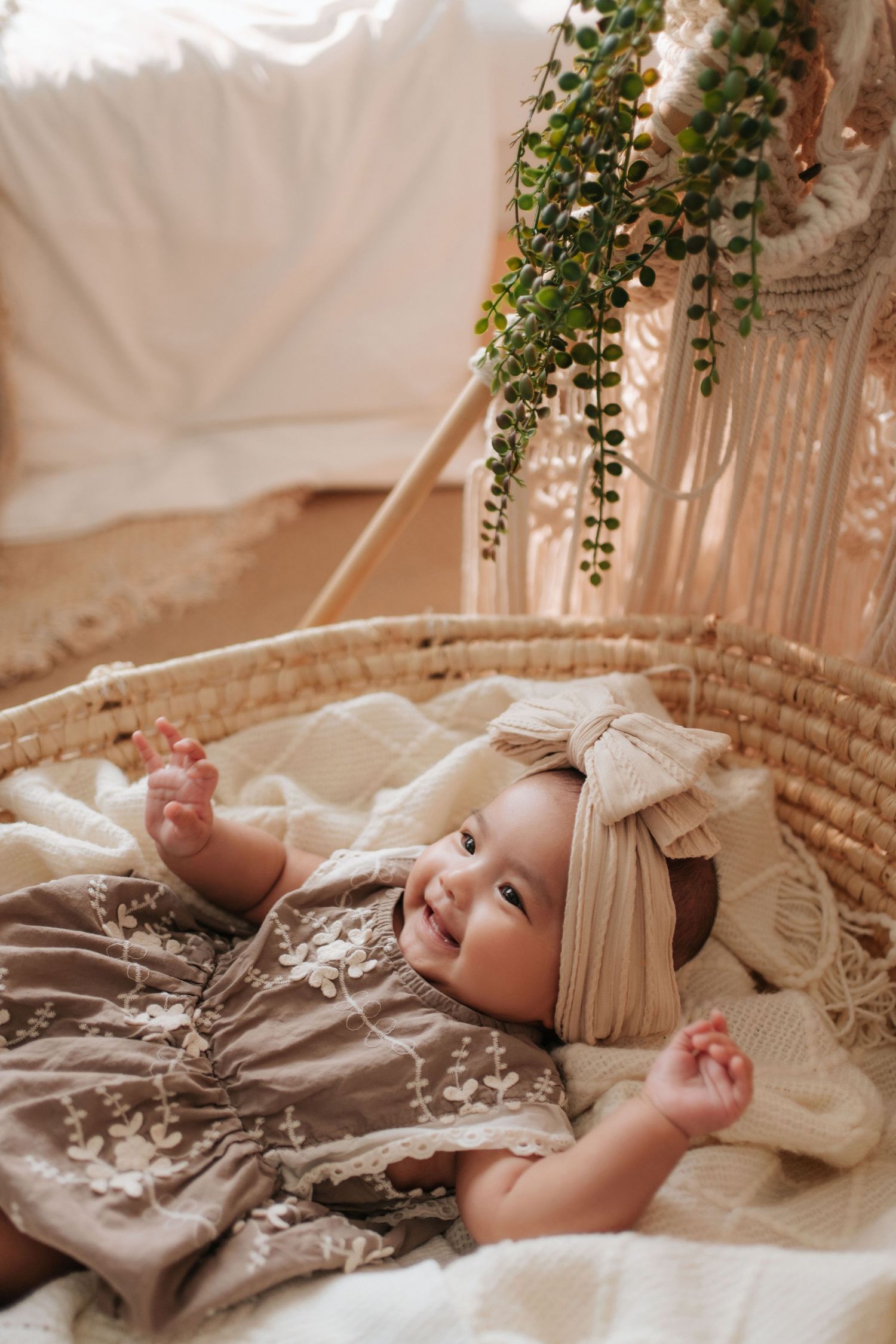 A baby rests on soft textured bedding surrounded by delicate vines and cream-colored fabric in a dreamy setting.一個嬰兒安詳地躺在米色的床單上，周圍環繞著嬌嫩的綠植和柔