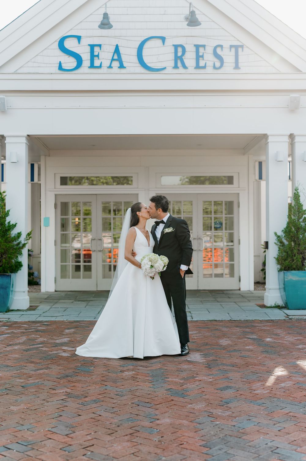 Bride and groom share a kiss in front of the Sea Crest venue entrance on their wedding day.