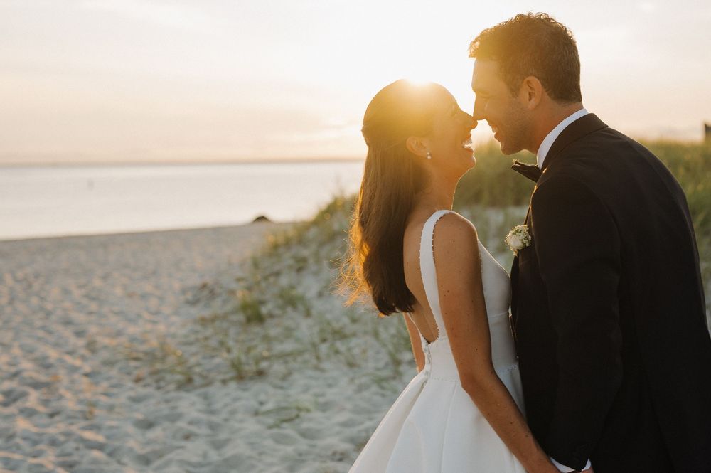A couple in wedding attire shares a romantic moment on a sandy beach at golden sunset.