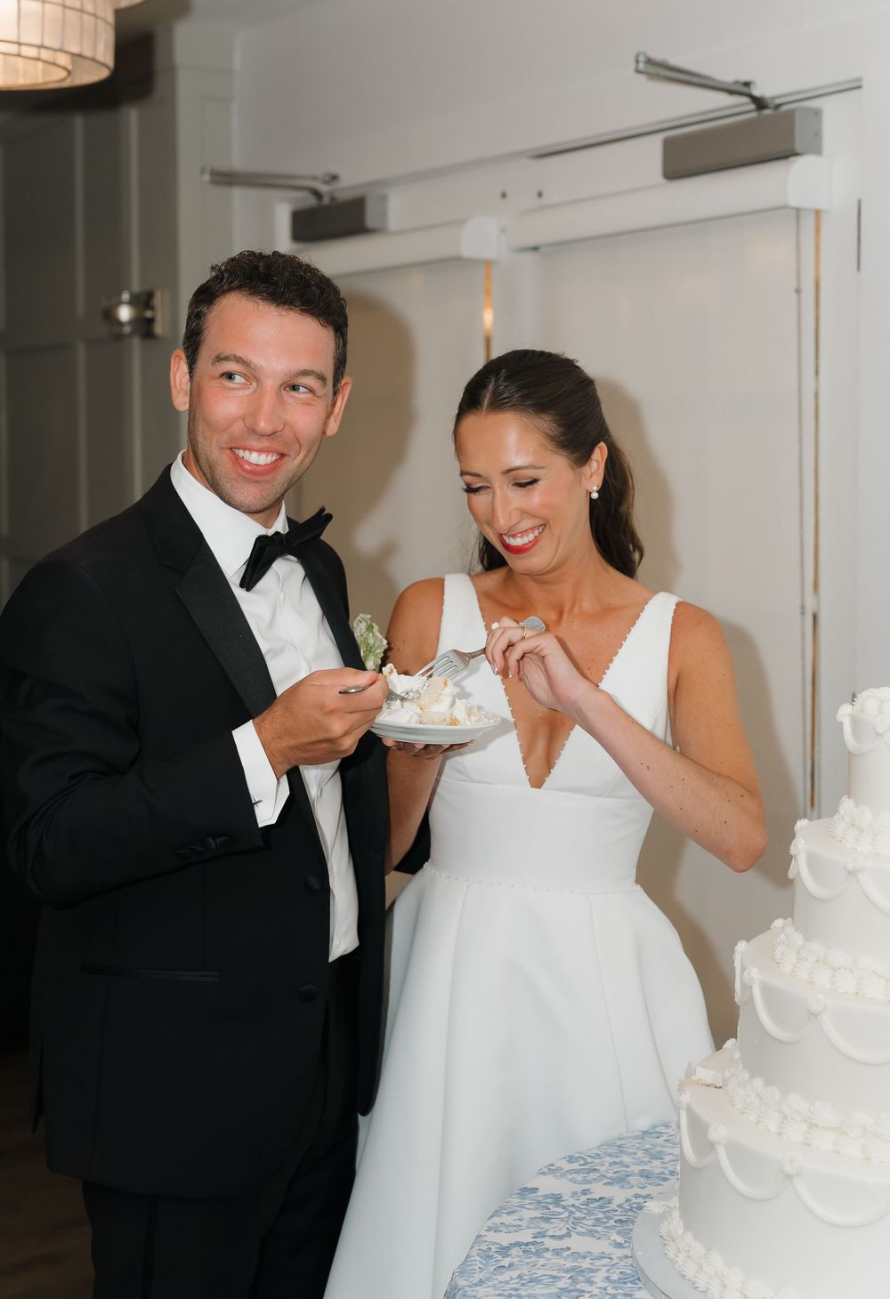 Bride and groom smiling while cutting their white wedding cake, dressed in formal attire at their wedding reception.