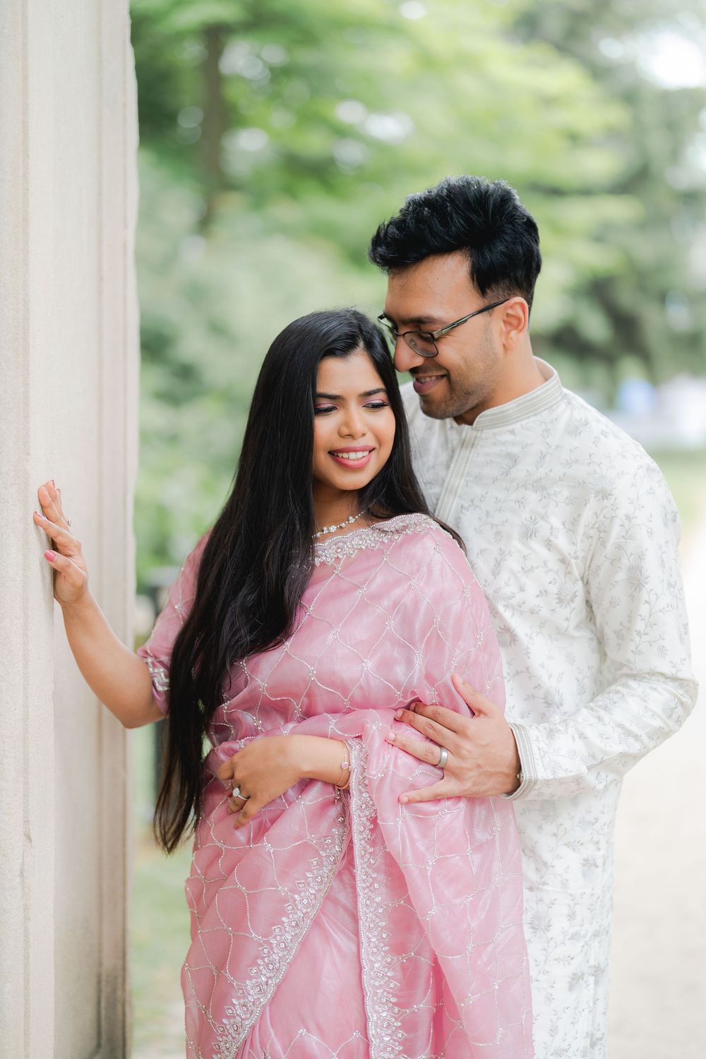 Couple in traditional Indian attire, woman in pink saree and man in white kurta, sharing a romantic moment outdoors.