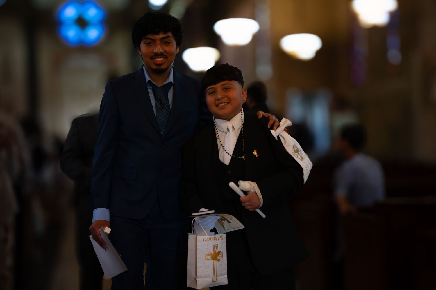 Two men in formal attire smiling together inside an ornate church during a ceremony.