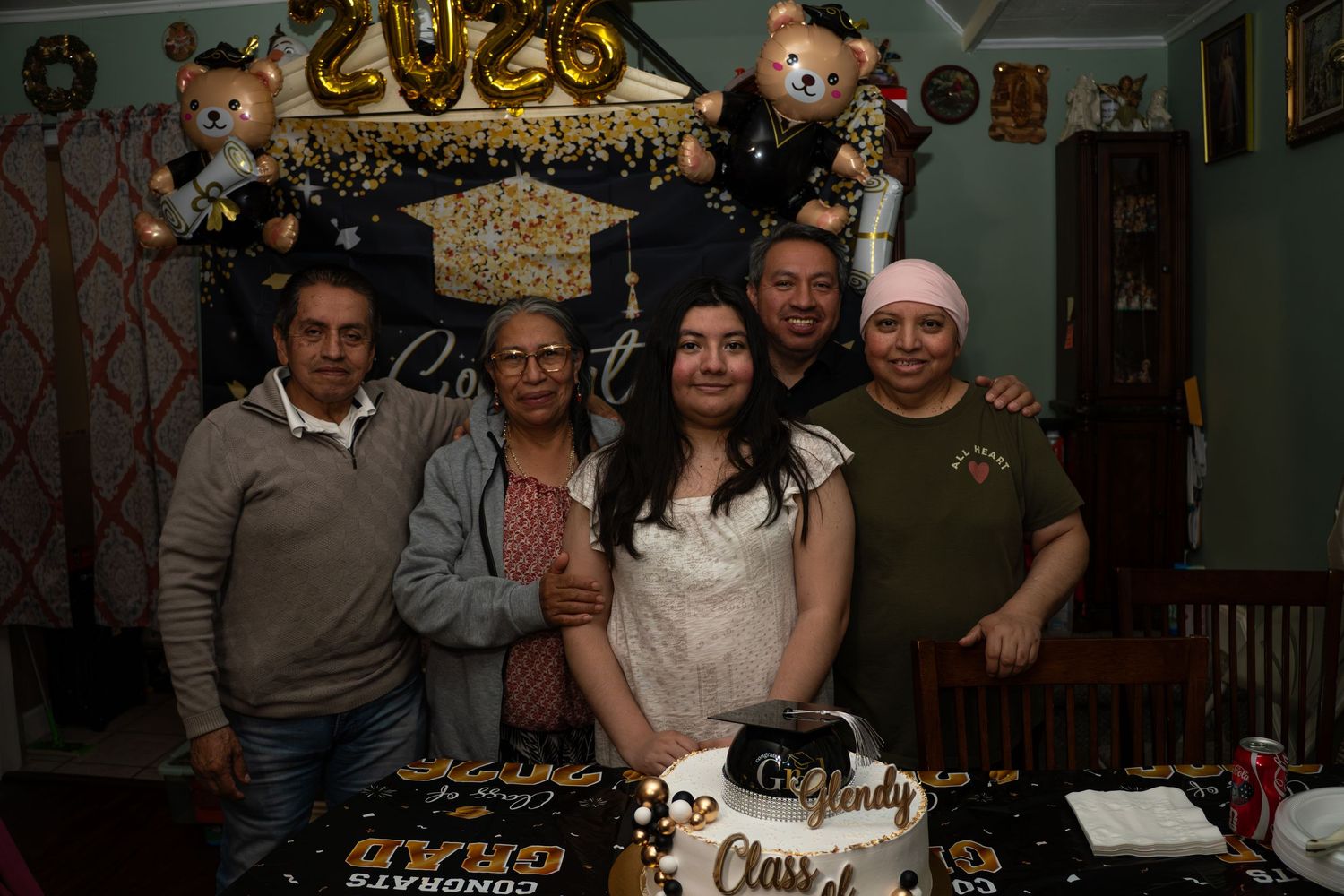 Family group celebrating graduation with Class of 2026 cake and decorations indoors at home party.