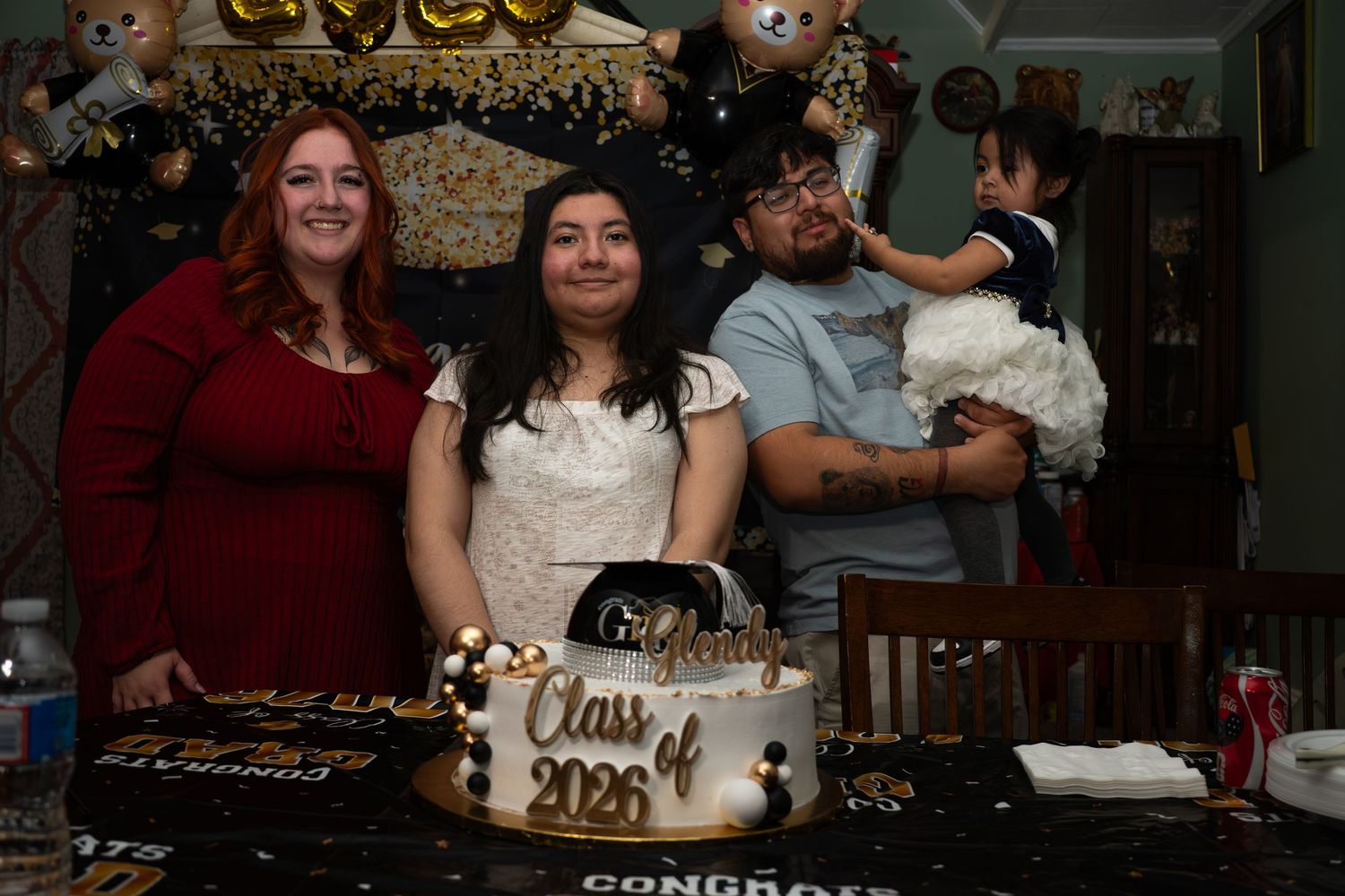 Family poses with Class of 2026 graduation cake at a celebratory party with decorations.