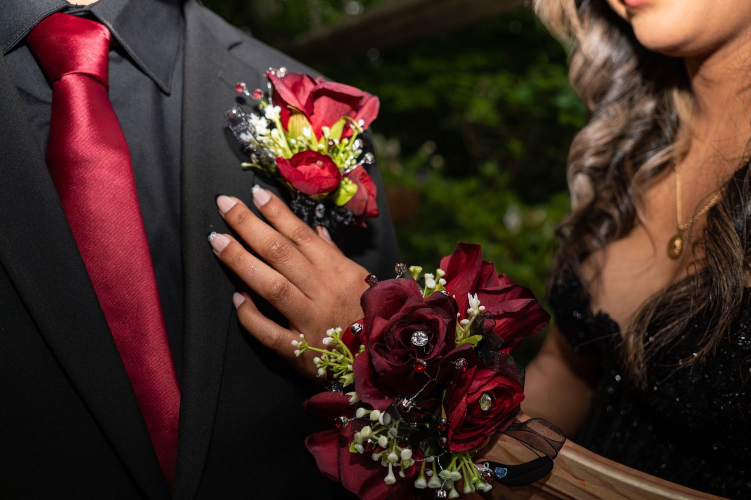 Close-up of prom couple with red rose boutonniere and matching corsage on black formal attire.