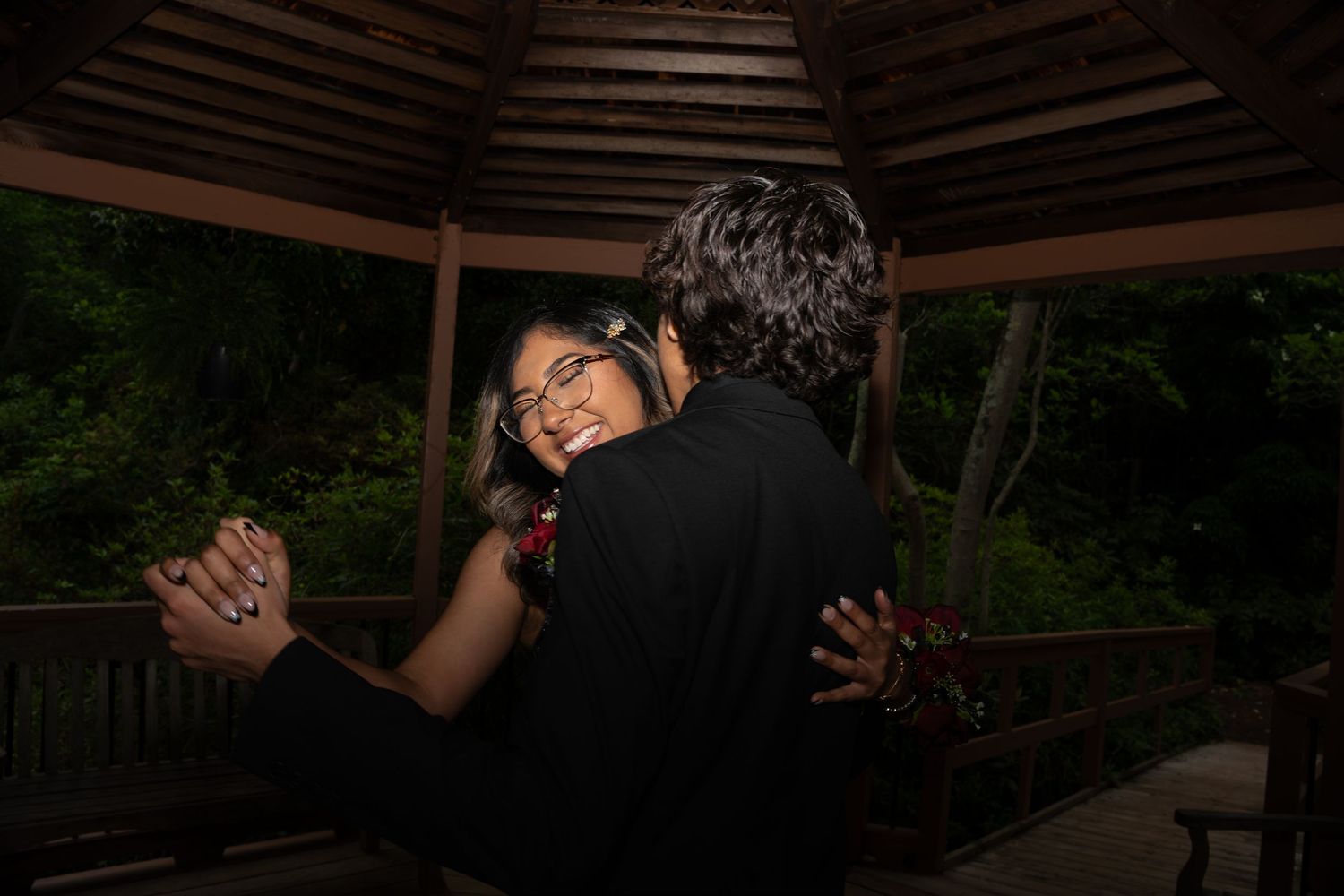 Couple sharing a romantic dance embrace in a wooden gazebo at prom night.