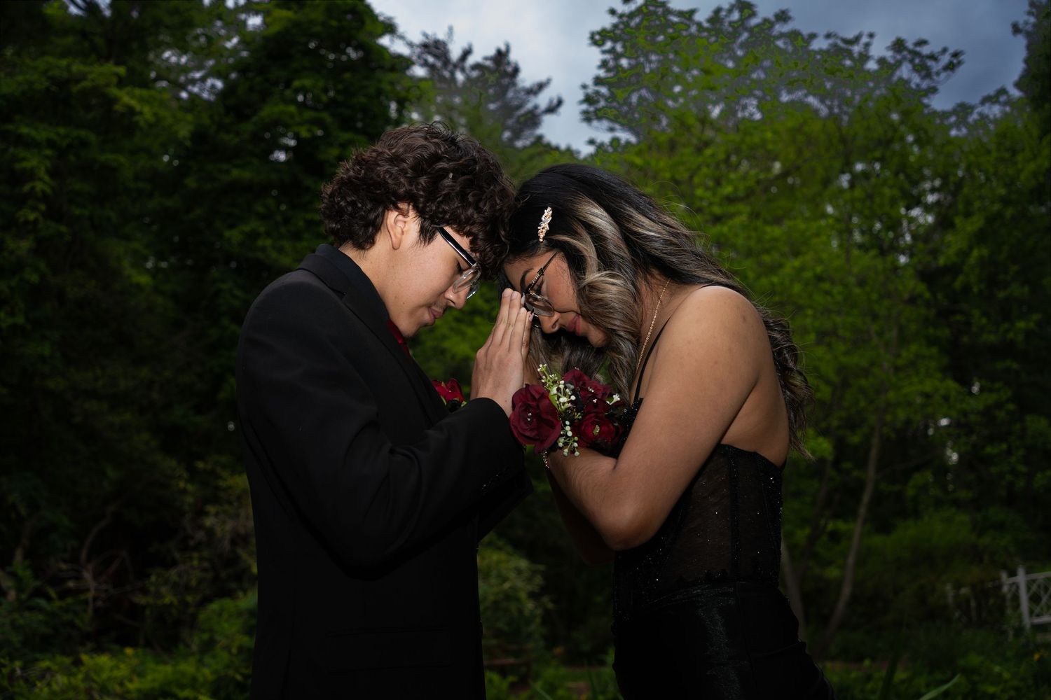 A couple in formal attire shares a romantic moment outdoors, with the young man kissing her hand at prom.