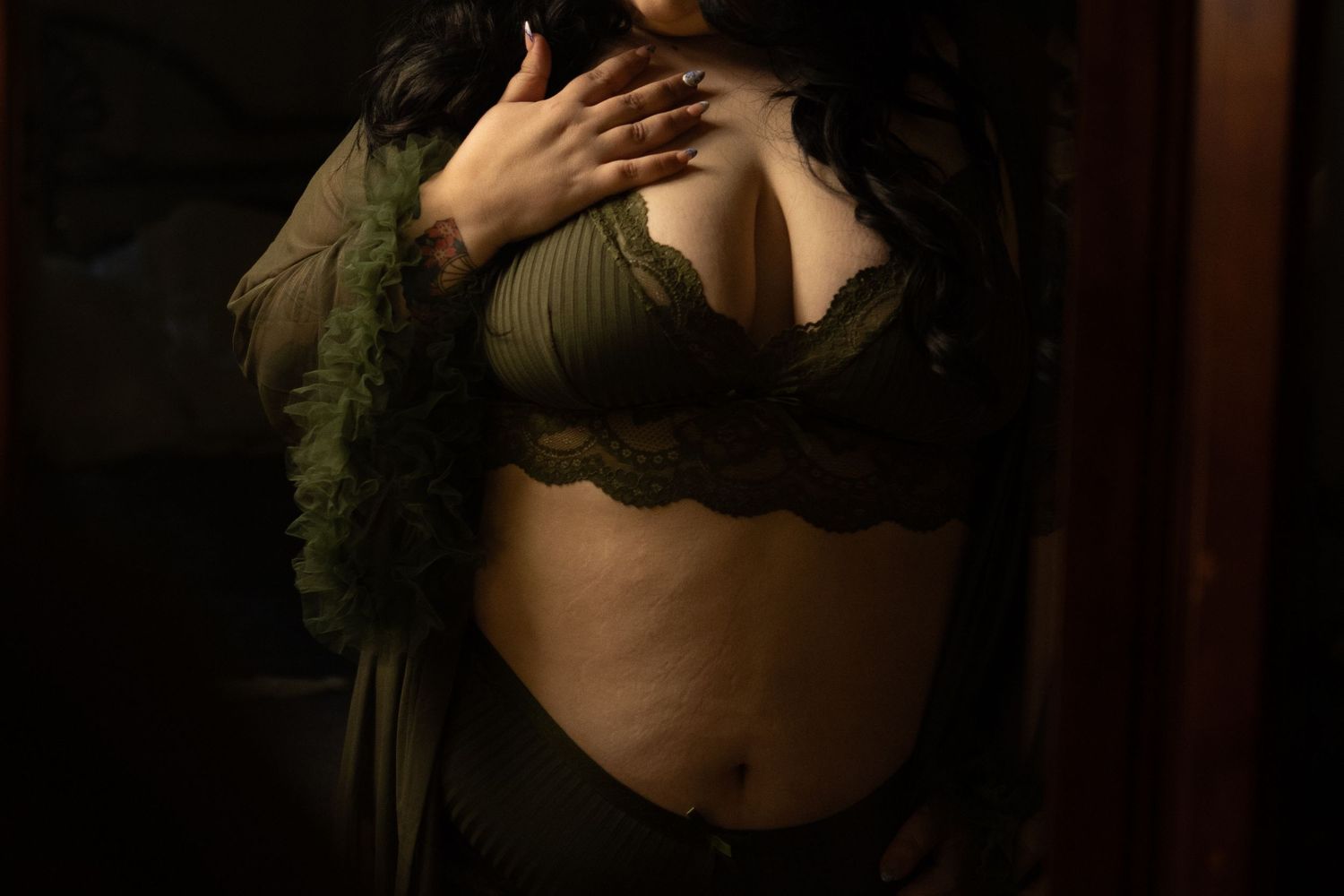A woman in red lace lingerie looking at herself sitting for a boudoir session with Jenna Bowman