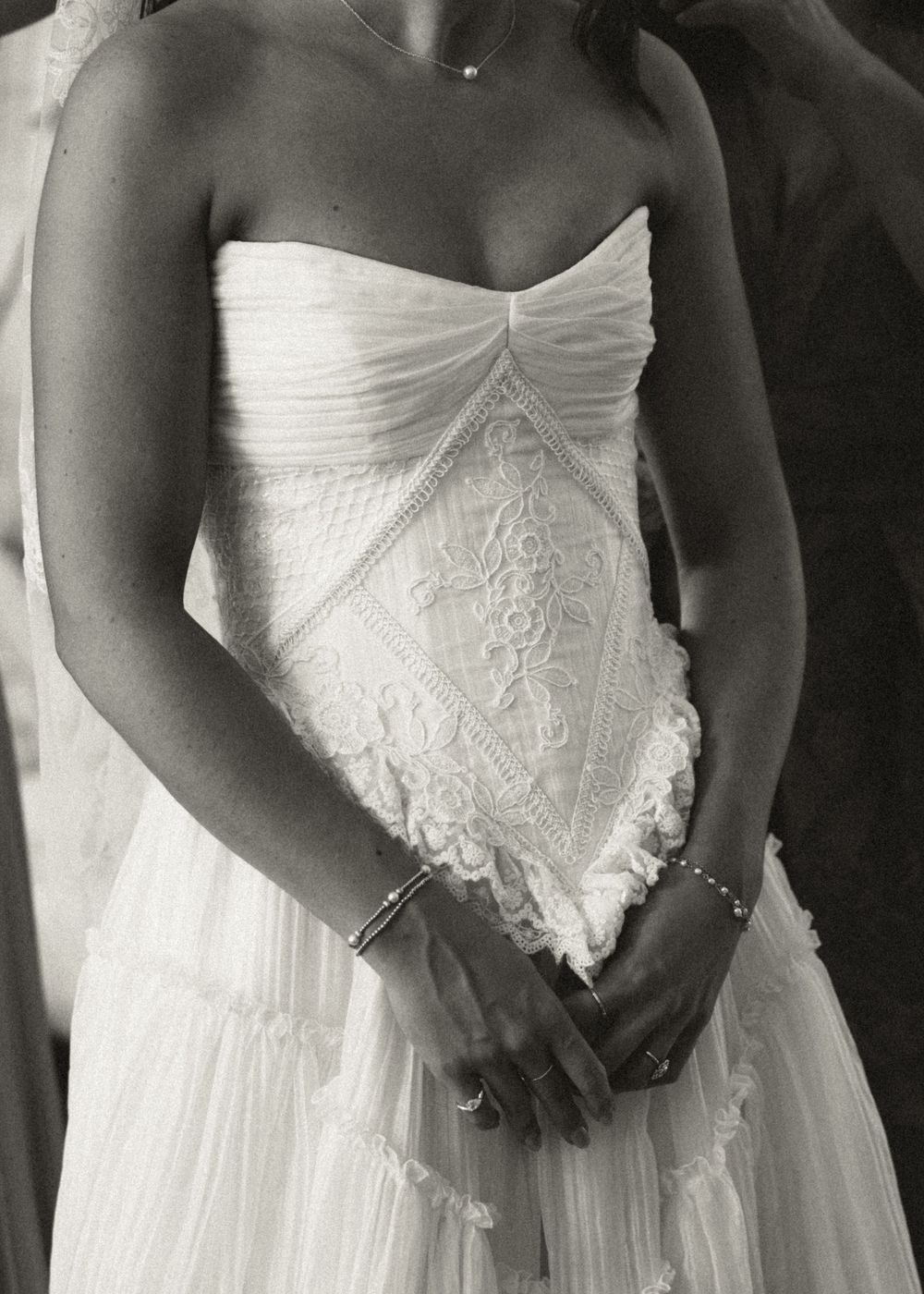 Black and white photo of a bride in a strapless lace wedding gown with intricate embroidery, wearing a delicate bracelet.