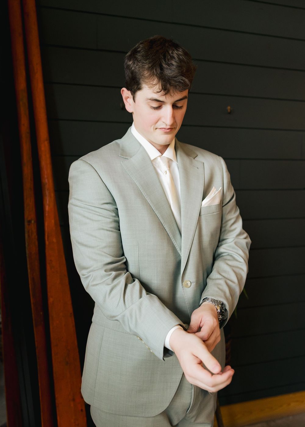Groom in light gray suit adjusting cufflinks before wedding ceremony.