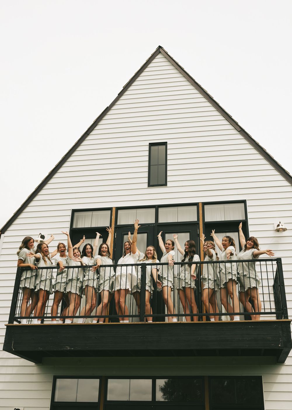 Group of bridesmaids in matching robes celebrating on a white A-frame building balcony.