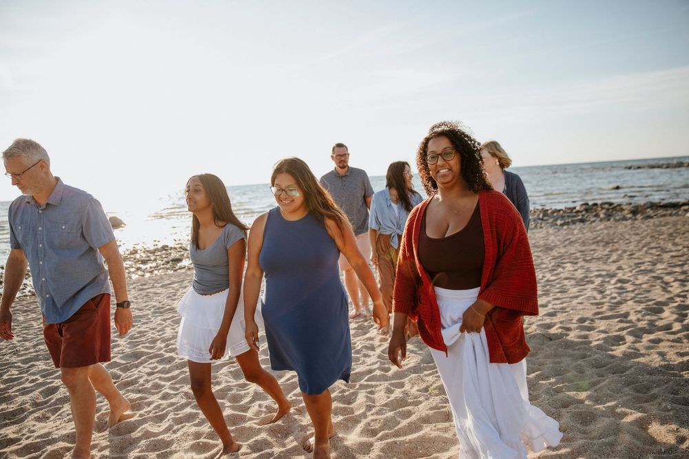 Group of friends walking together on a sunny beach, wearing casual summer outfits in red, blue, and white.
