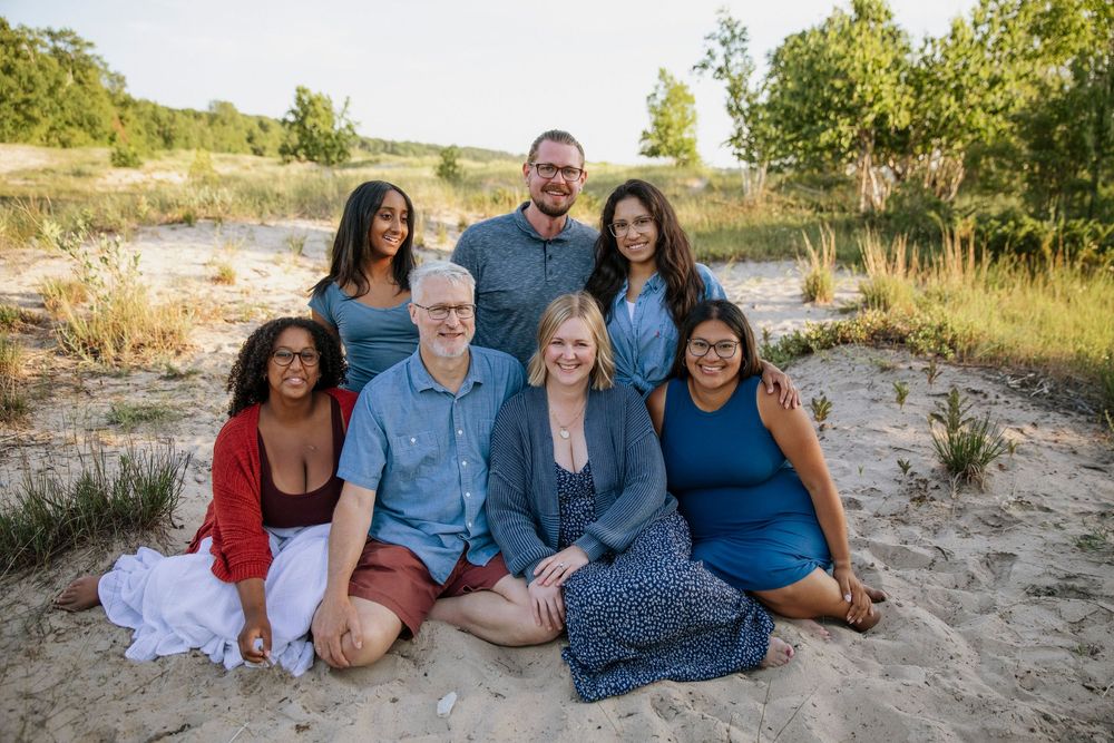 Family of seven smiling together on sandy beach dunes during golden hour outdoor portrait session.