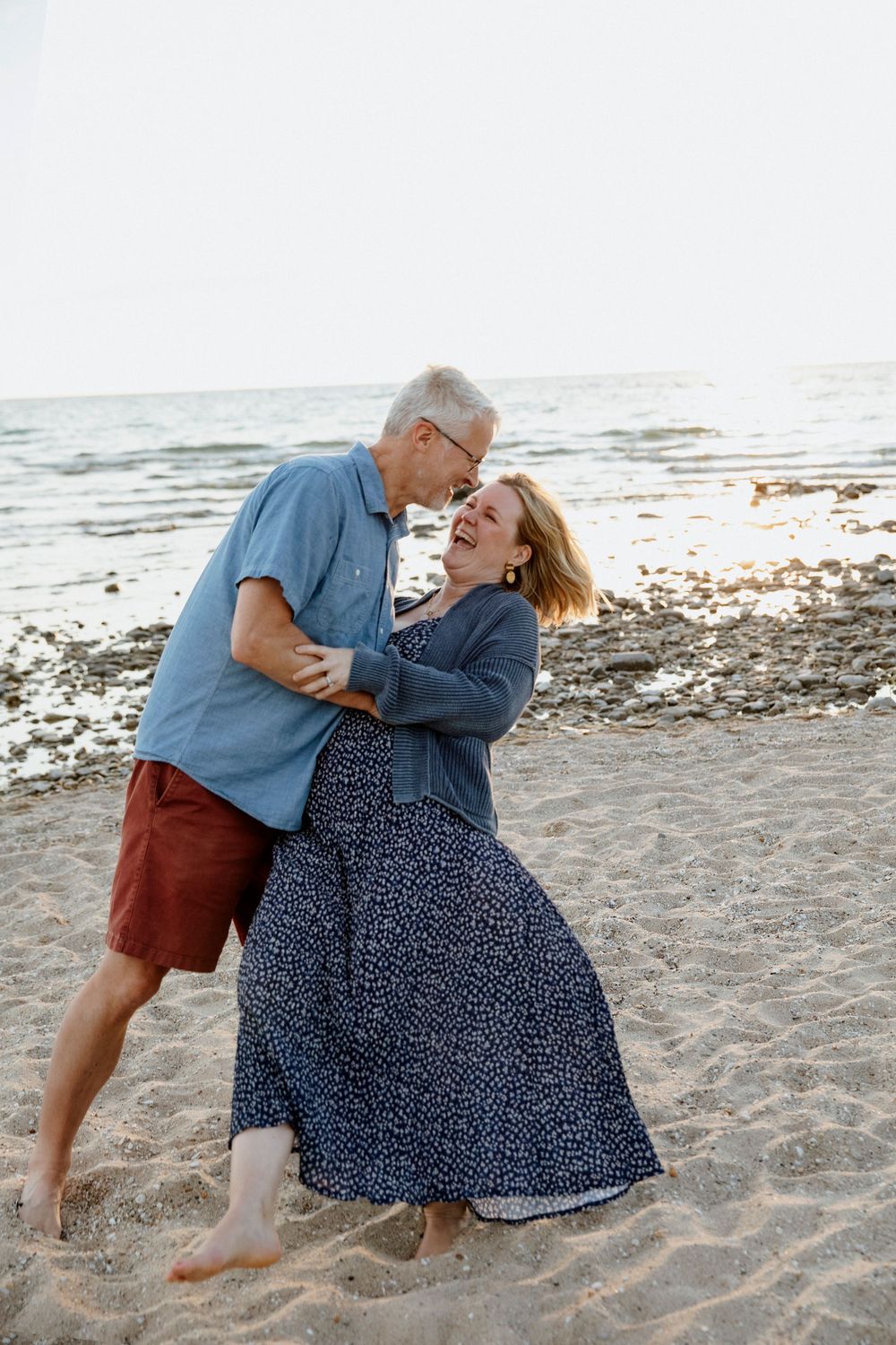 Happy mature couple dancing and laughing together on a sandy beach near the ocean on a sunny day.