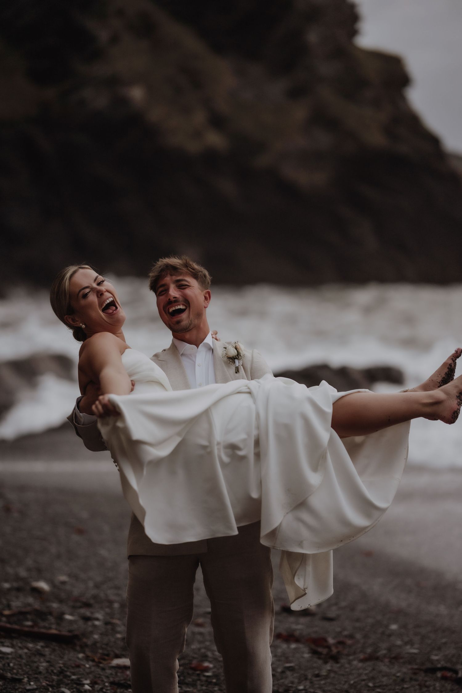 Couple laughing together during a beach photoshoot at Tunnels Beach, capturing a candid and joyful moment