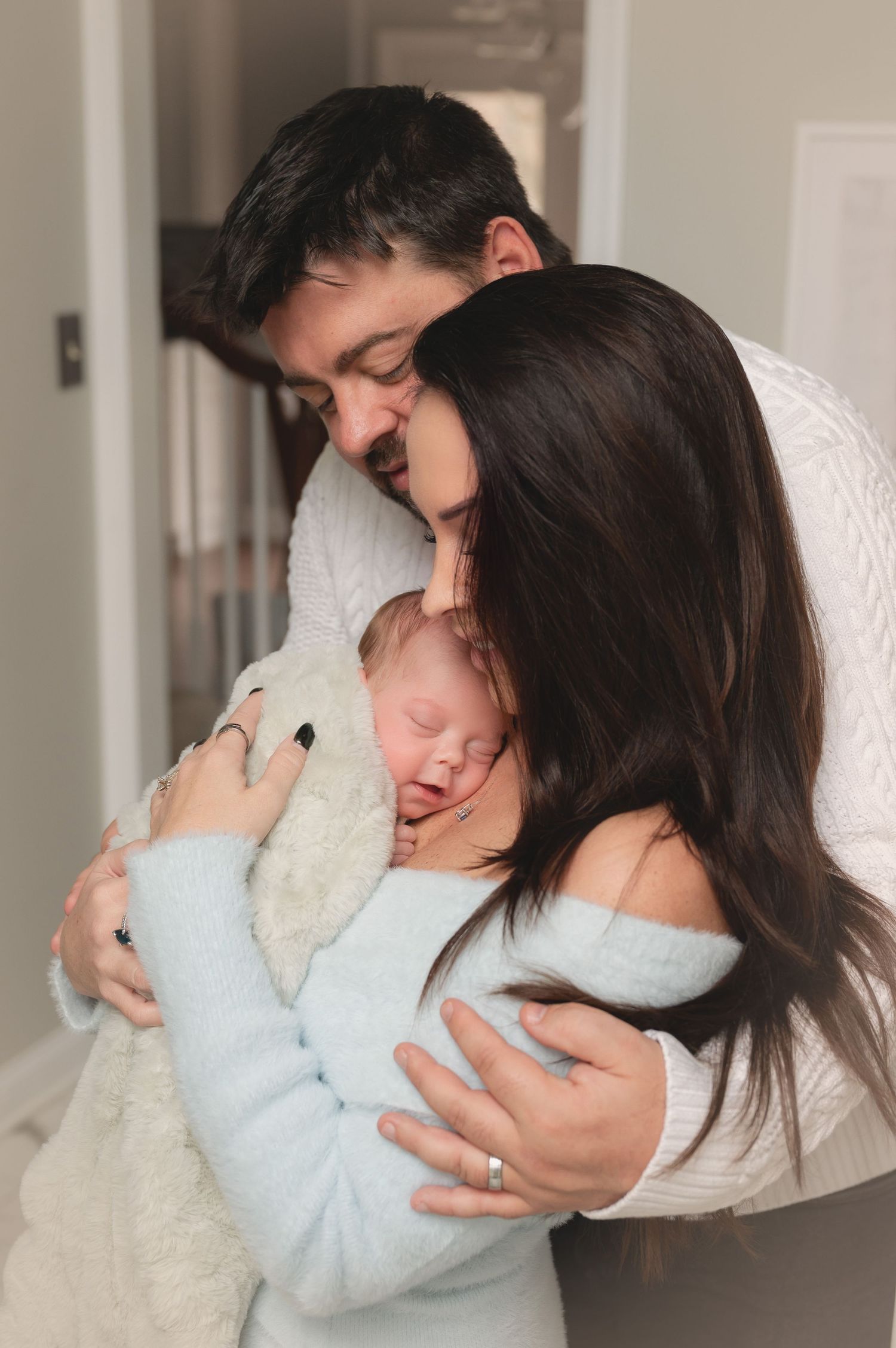 A series of tender moments showing parents embracing and cuddling with their newborn baby wrapped in a light blue blanket.