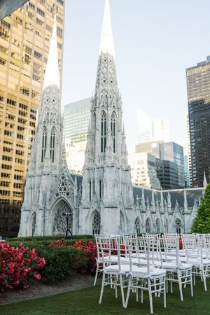 White chairs arranged on a rooftop garden with St. Patrick's Cathedral and NYC skyscrapers in the background.
