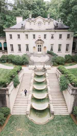 Aerial view of an elegant Georgian mansion with cascading stone fountains, grand staircases, and lush greenery surrounding the estate.