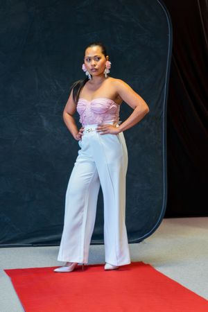 Woman in pink corset top and white wide-leg pants posing on red carpet with floral earrings.