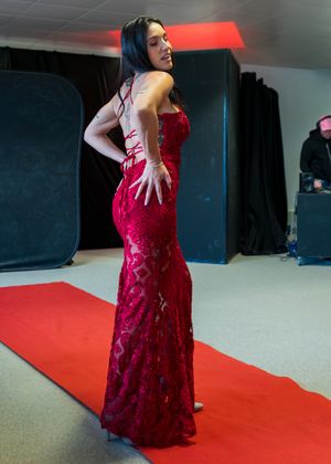 Woman in elegant red sequin mermaid gown posing on red carpet in a studio setting.