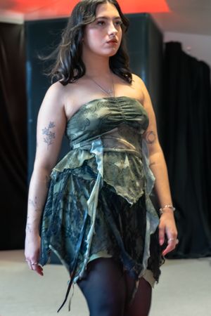 Woman in green strapless fairy-style dress with tattoos walks a fashion runway wearing black tights.