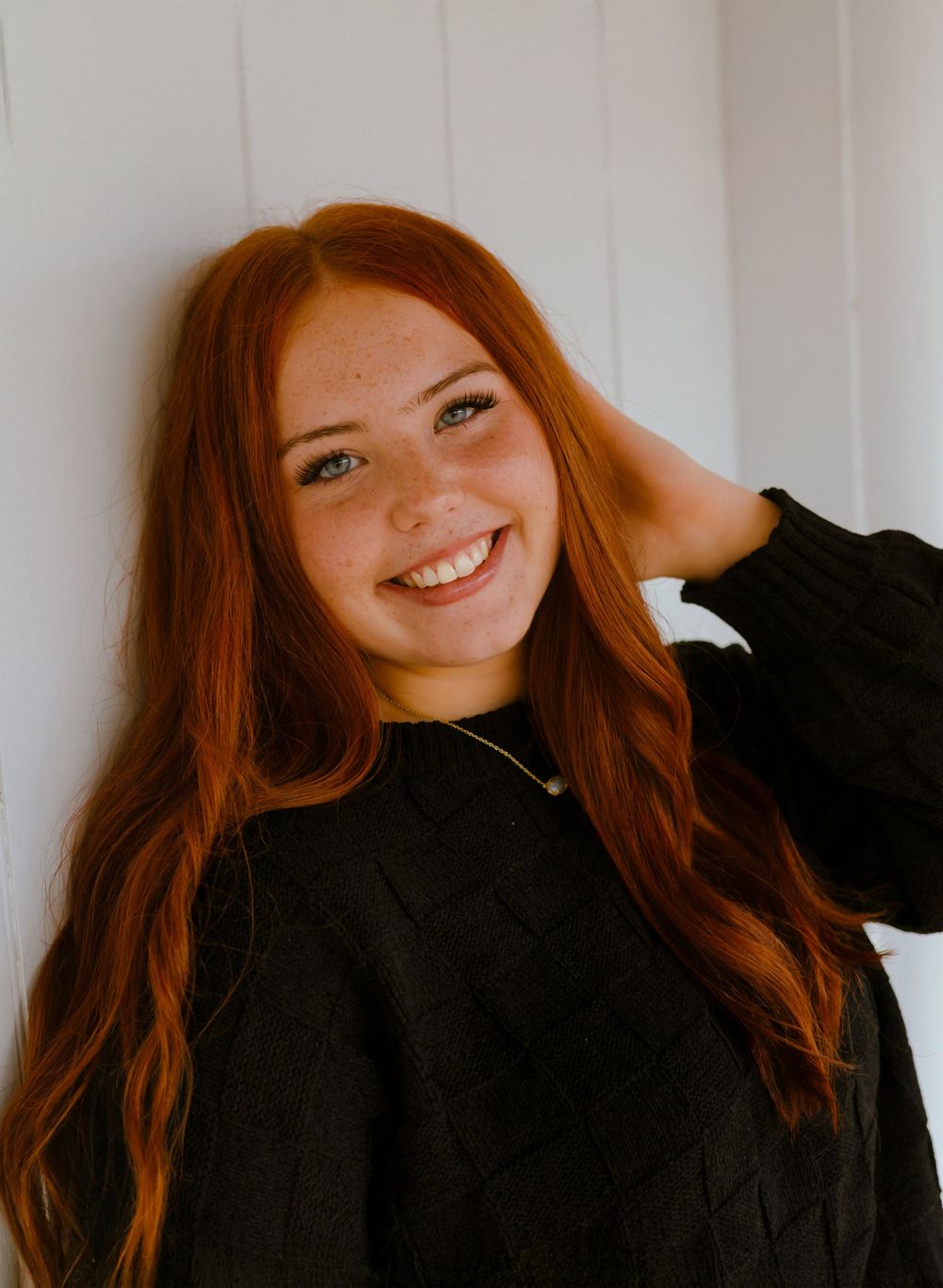 A series of four photos showing someone with long red hair in a black sweater posing against a white wall.