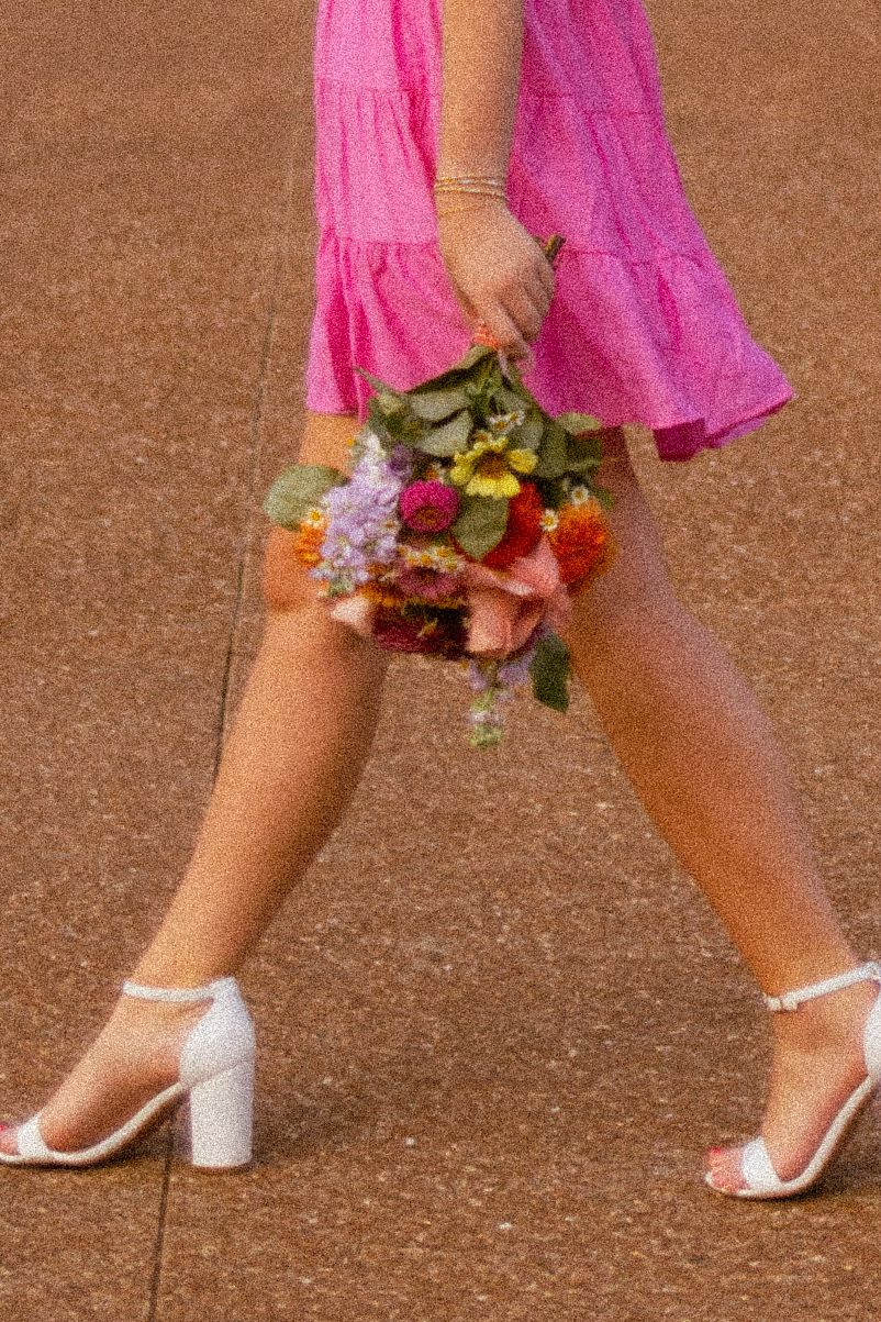 A sequence of walking feet in white sandals and pink dress hem shows graceful movement across a brown surface.